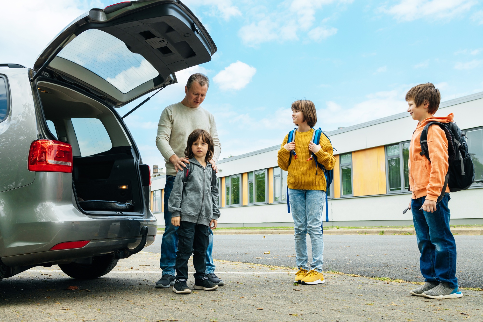 Dad escorts his children to school, father takes school bags out of the car.
