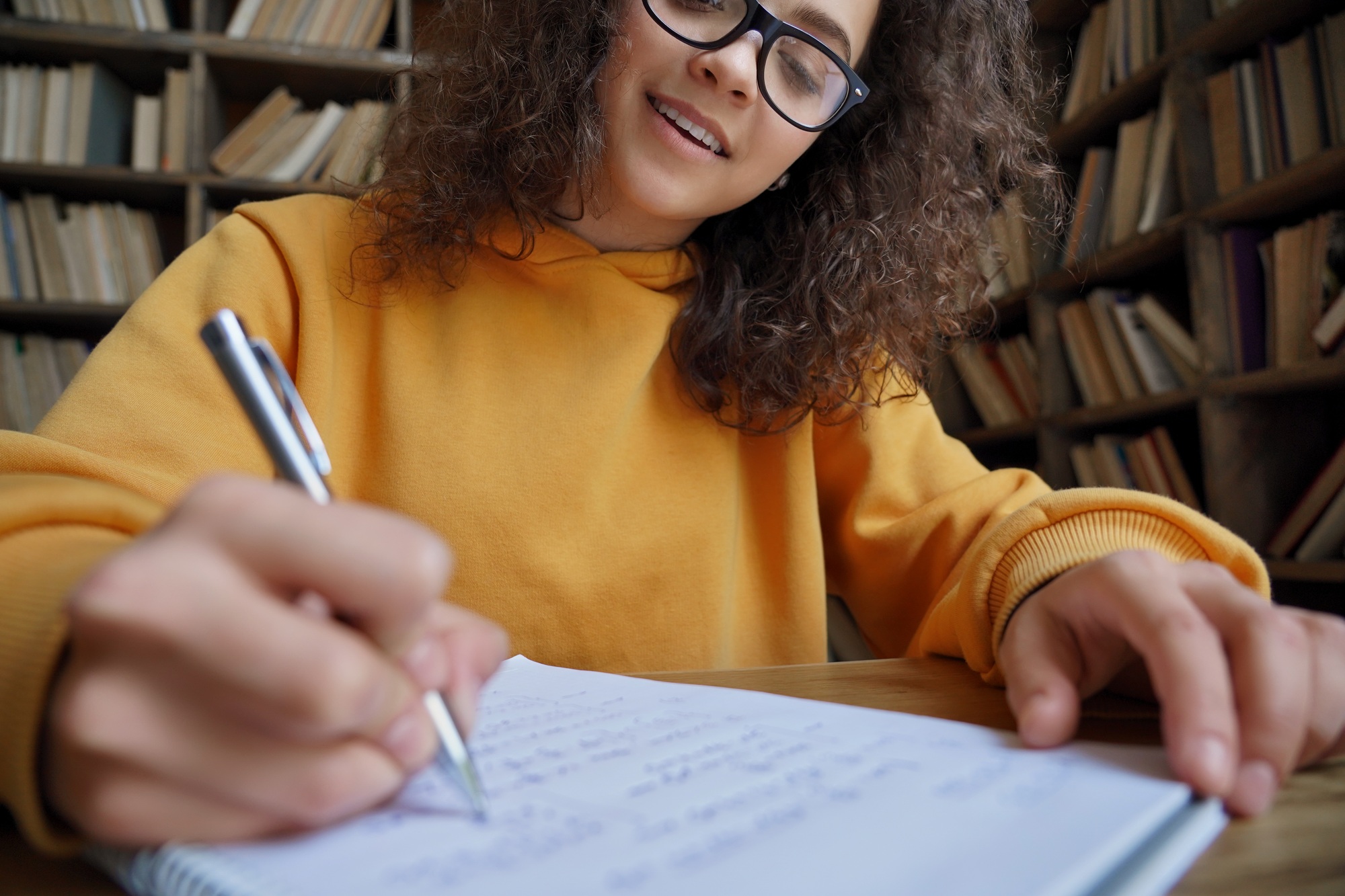 Hispanic teen girl student writing in workbook doing homework, close up.