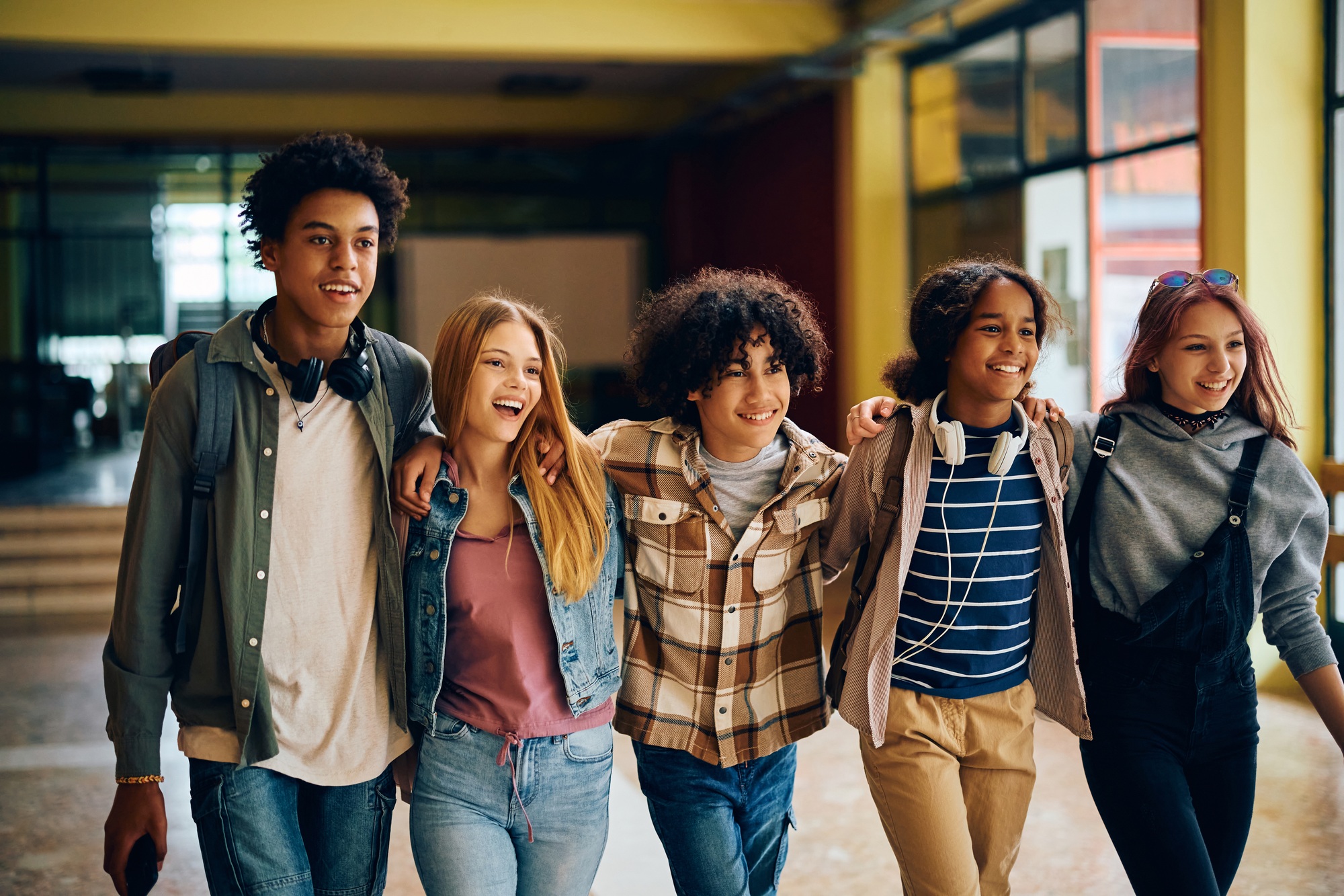 Cheerful high school students walking embraced through the hallway.