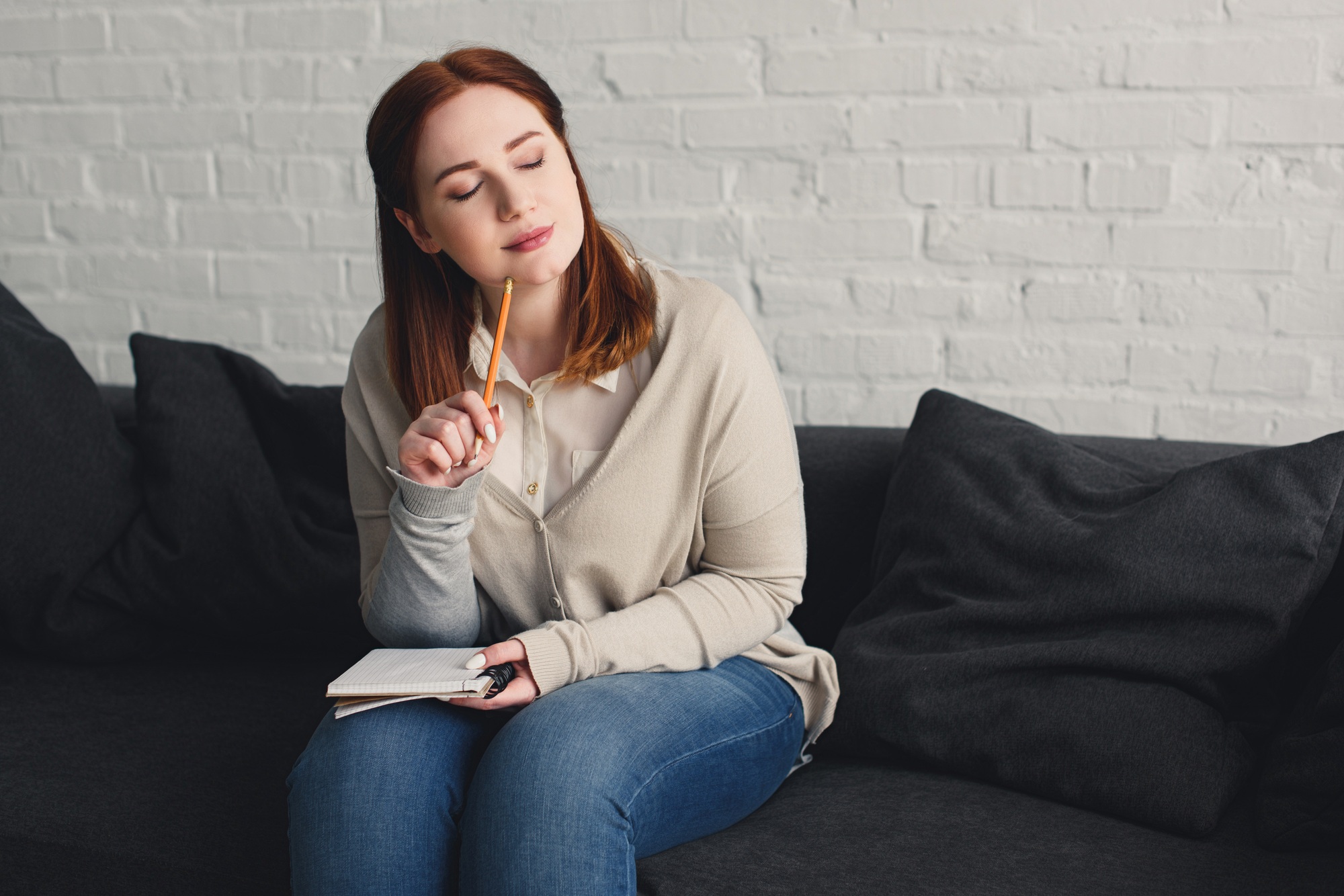 pensive beautiful girl with closed eyes touching chin with pencil at home