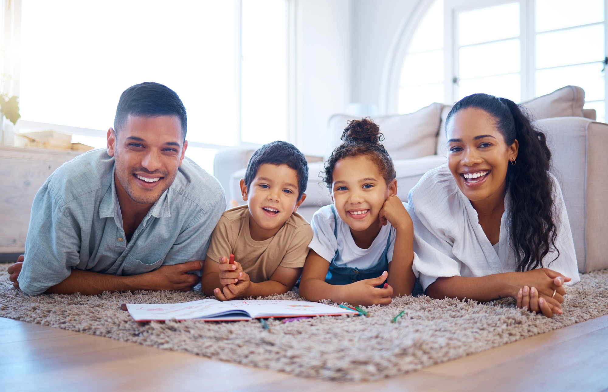 Portrait of a smiling young mixed race family lying close together on the living room floor at home