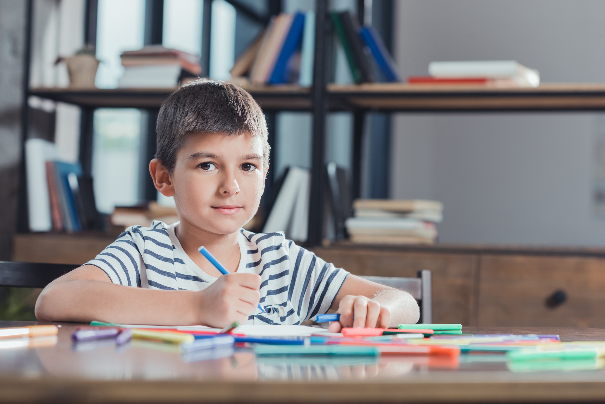 portrait of boy drawing picture with colorful markers at table at home
